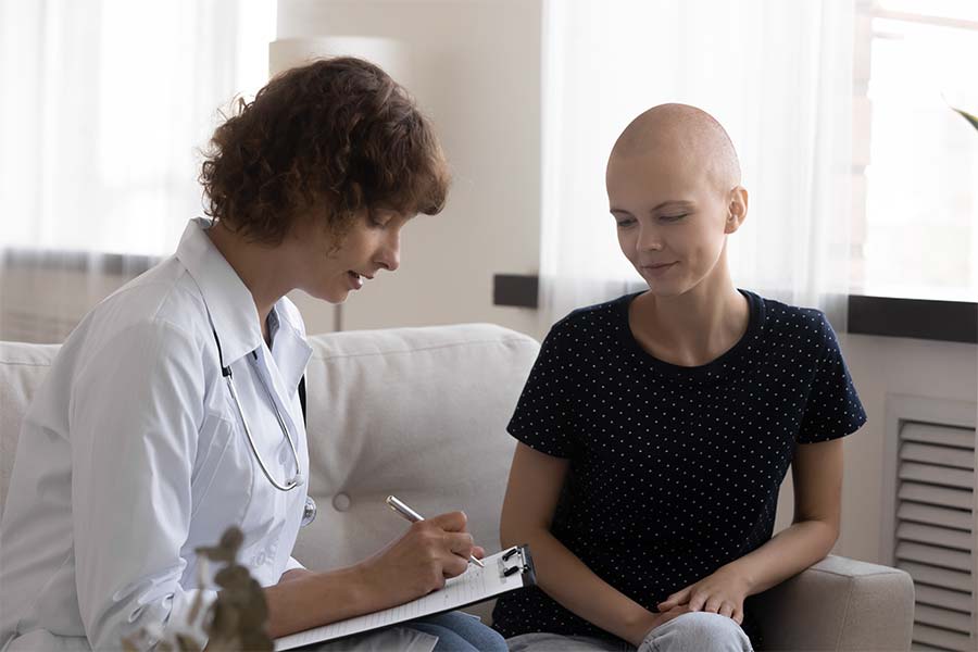 A young woman with a shaved head talking with a clinician who is taking notes on a clip board.